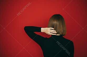 The back of a stylish girl in a black sweater on a red background, straightens short hair with a bob hairstyle. Woman with bob