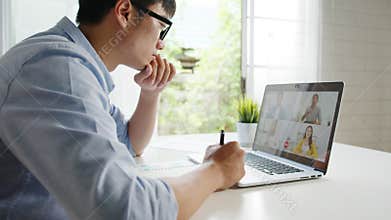 Young Asia businessman using laptop talk to colleagues about plan in video call meeting while work from home at living room. Self-