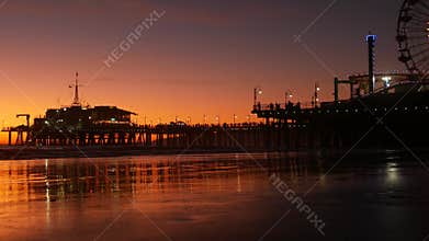 Twilight waves against classic illuminated ferris wheel, amusement park on pier in Santa Monica pacific ocean beach