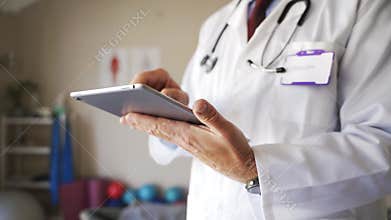 Elderly Caucasian doctor in lab coat writing results on clipboard in practice or clinic