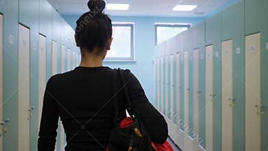 Girl walks carrying sports bag along gym dressing room
