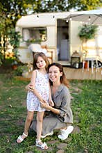 Young woman kissing daughter near house on wheels.
