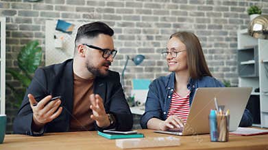 Male and female coworkers discussing work sitting at desk with laptop together