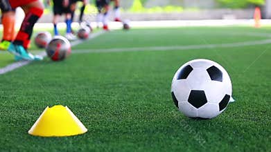 Soccer ball on green artificial turf between cones maker with blurry soccer team training