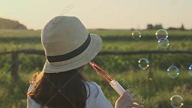 Beautiful child girl in a hat blowing soap bubbles