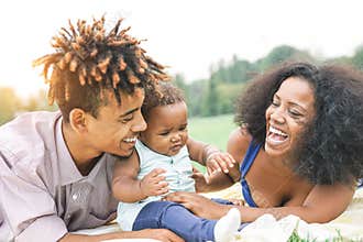 Happy African family enjoying a picnic sunny day outdoor - Mother and father having fun with their daughter in a public park