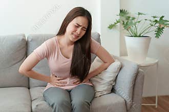 Asian woman with menstruation and pain period cramps. young women having painful sitting on sofa at her home