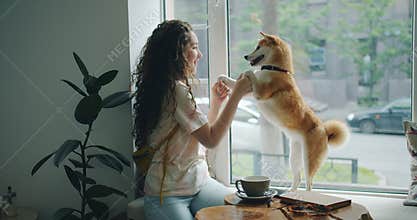 Happy young woman dancing with pet dog sitting on window sill in cafe having fun