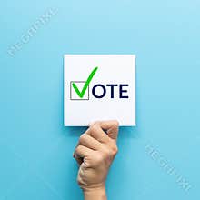 Hand holding white paper with the `vote` and green check mark voting symbols in checkbox of the inscription isolated on blue