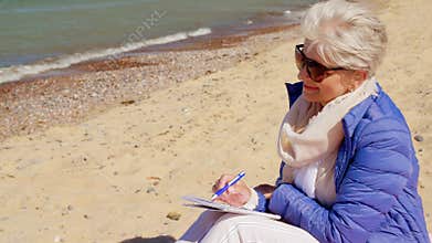 Senior woman writing to notebook on summer beach