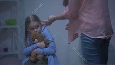 Angry mother screaming on daughter hugging teddy bear behind rainy window