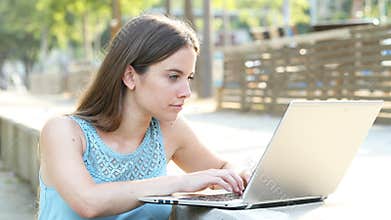 Serious woman writing on laptop in a park