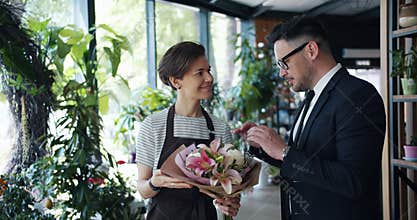 Female florist talking to male customer holding bunch of flowers in store