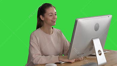 Happy woman having a video call sitting in front of her computer on a Green Screen, Chroma Key.