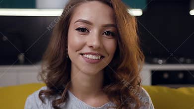 Lovely jolly young woman with cute smile posing on camera on the home interier background