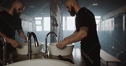 Sad athletic Caucasian young man washing hands and face alone in dark gym locker room, motivation crisis slow motion.