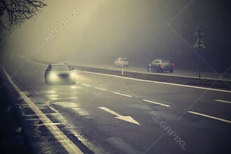 Cars in the fog. Bad winter weather and dangerous automobile traffic on the road. Light vehicles in foggy day