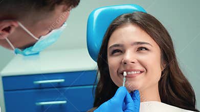 Smiling brunette patient woman having appointment in dental clinic dentist in mask and gloves applies enamel scale to