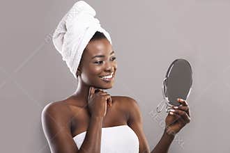 Attractive black woman holding mirror and looking at her perfect skin