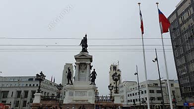 Street market with people walking, in Sotomayor square, monument of Arturo Prat and on the seafr