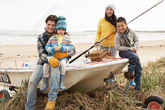 Family Sitting On Boat With Fishing Rod On Beach
