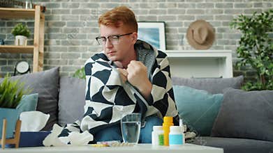 Sick teenager couching sneezing in paper tissue on couch covered with blanket