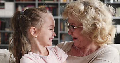 Happy older grandma hug cuddle cute granddaughter look at camera