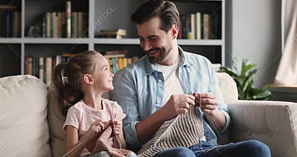 Happy young father having fun teaching little daughter knitting needles