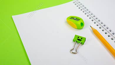 School Notepad with Yellow Pencil, Pencil Sharpener, Smile Binder Clip on Green Background