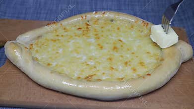 Woman's hand smears  butter khachapuri with fork