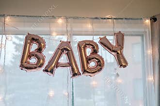 Baby shower letter balloon decor hanging by a window