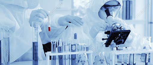 Analysing sample with microscope with another scientist holding coronavirus covid-19 blood sample tube on hand in laboratory