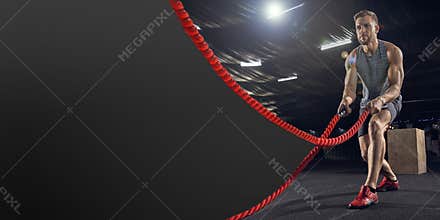 Young healthy man athlete doing exercise in the gym with ropes, flyer with copyspace