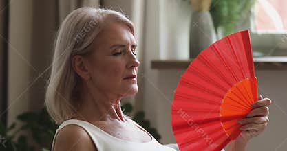 Overheated old senior woman feeling hot wave fan at home
