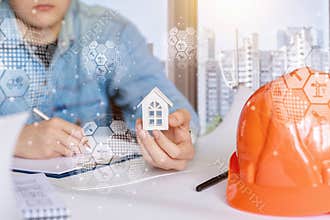 A civil engineer holding a house model and operates with the technical documentation