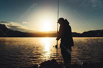 Silhouette fisherman wirh fishing rod at sunrise sunlight, outline man enjoy hobby sport on evening lake, person catch fish