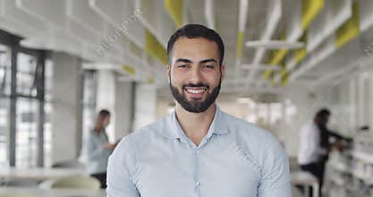 Front view of it trainee looking to camera and smiling at coworking zone. Young startup founder looking happy and