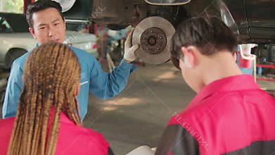Supervisor engineer is teaching mechanic workers about car repair at a garage.
