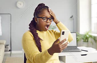 Beautiful africanamerican woman looks at the phone in horror.