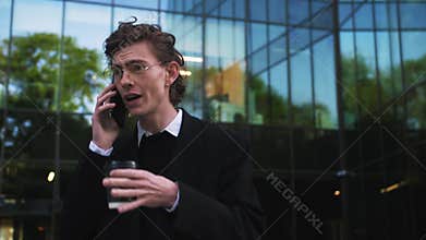Portrait worried annoyed serious young man standing outndoors talking on telephone answering call near modern office