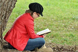 Pretty young teen girl reading book under big tree