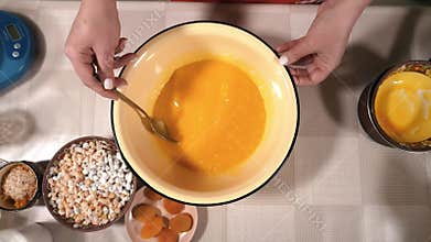 The hostess is preparing dough in the kitchen. Mixes beaten eggs with flour. Women's hands stir the mixture for