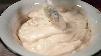 The hostess is preparing dough in the kitchen. Mixes beaten eggs with flour. Women's hands stir the mixture for