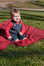 Six-month old boy on red blanket on grass