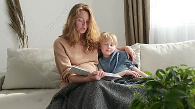Cute pregnant mom reading a book to her eldest son. Quality parenting time with children.