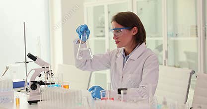 Concentrated female scientist in safety glasses shakes a glass flask with clean water