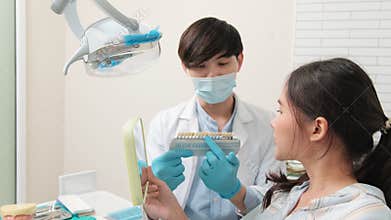 Asian male dentist explains teeth care to a female patient in a dental clinic.