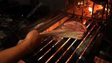 Raw piece of juicy T-bone meat stake, put into the open fire on a grill.