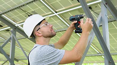 Male engineer in protective helmet installing solar photovoltaic panel system using screwdriver. Alternative energy