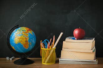 School supplies next to the globe and stack of books on the blackboard background